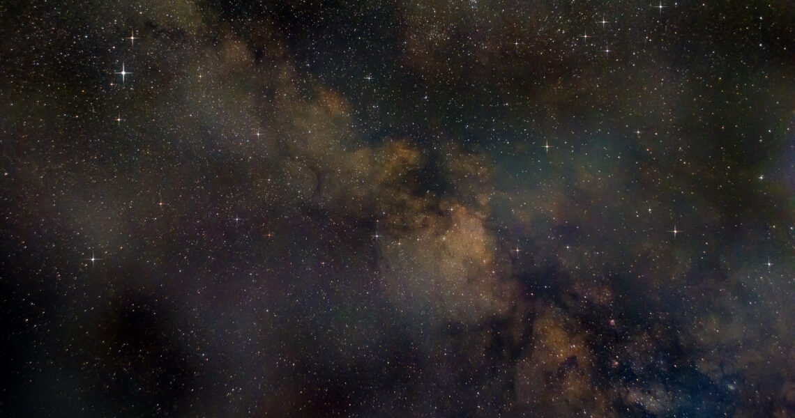 A view of the Milky Way rnning diaginally from top left to bottom right, showing shades of orange, red and blue. A number od stars are in view - the brightest to the top left is Altair